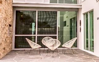 External view of tinted aluminium stacker doors with cane chairs placed in the front.